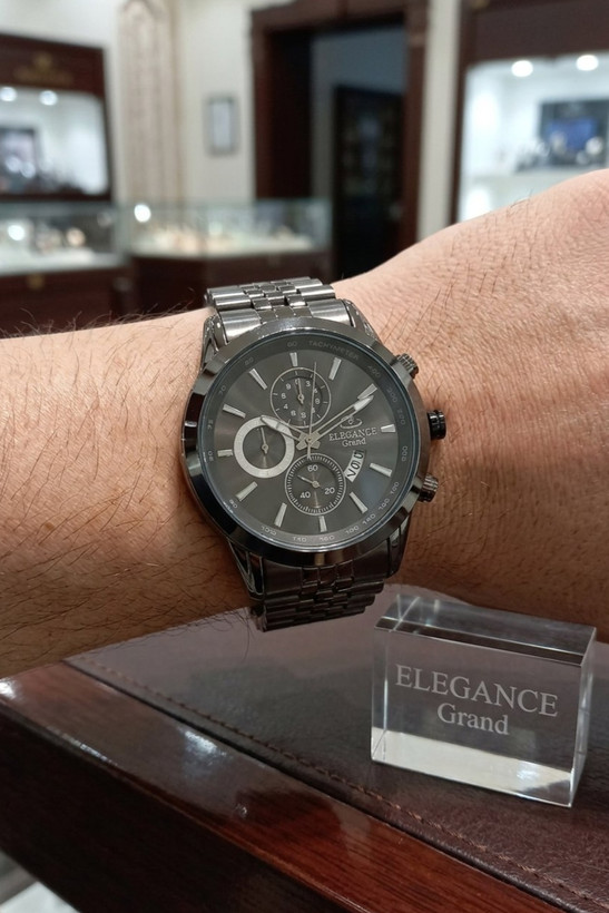ساعت مردانه الگانس گرند با نشانگرهای استیل روی مچ دست مردانه، کنار دیسپلی ELEGANCE Grand در فروشگاه ساعت